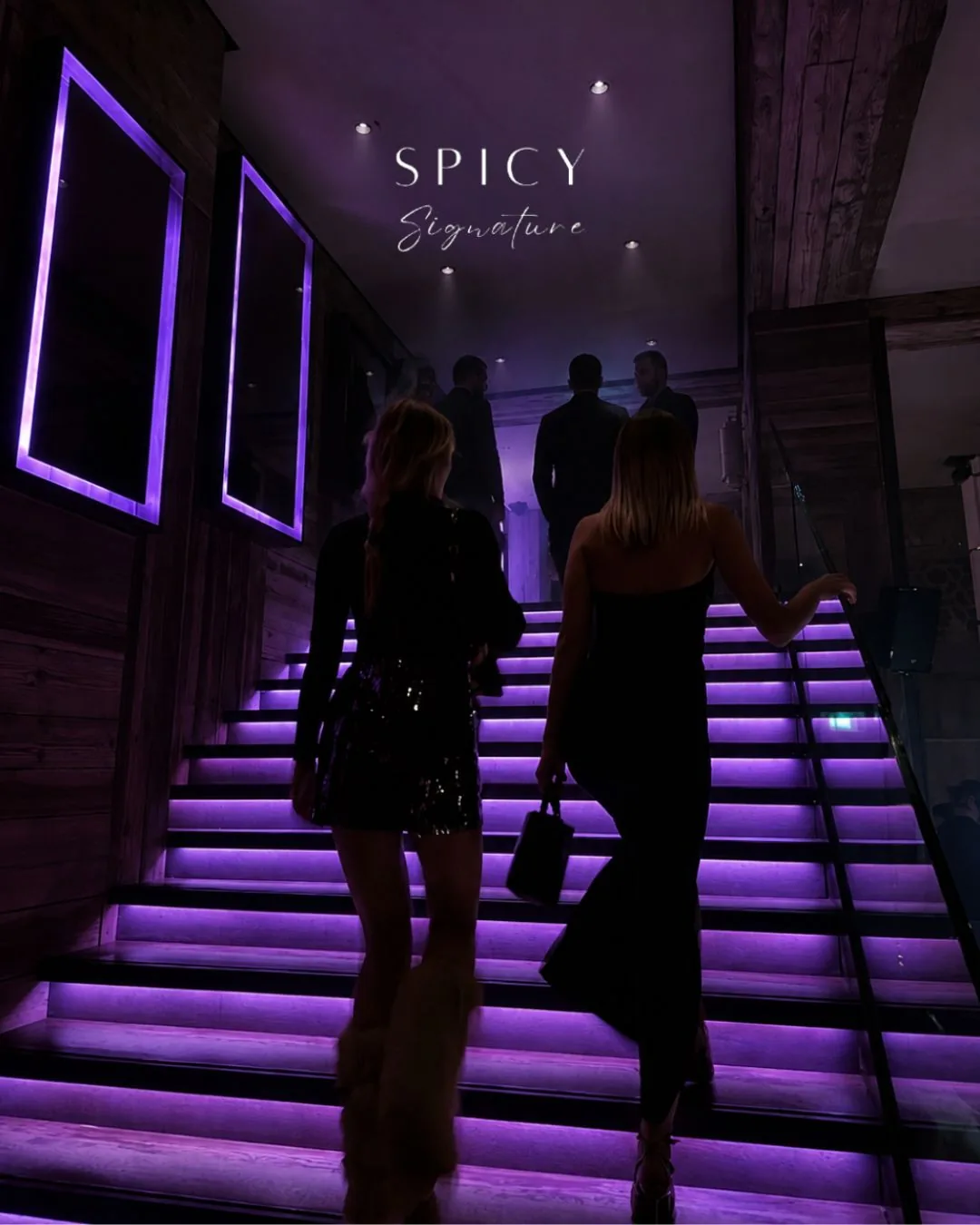 Dos invitadas de negro suben la escalera iluminada en morado al comienzo de una noche Spicy en Bogotá
